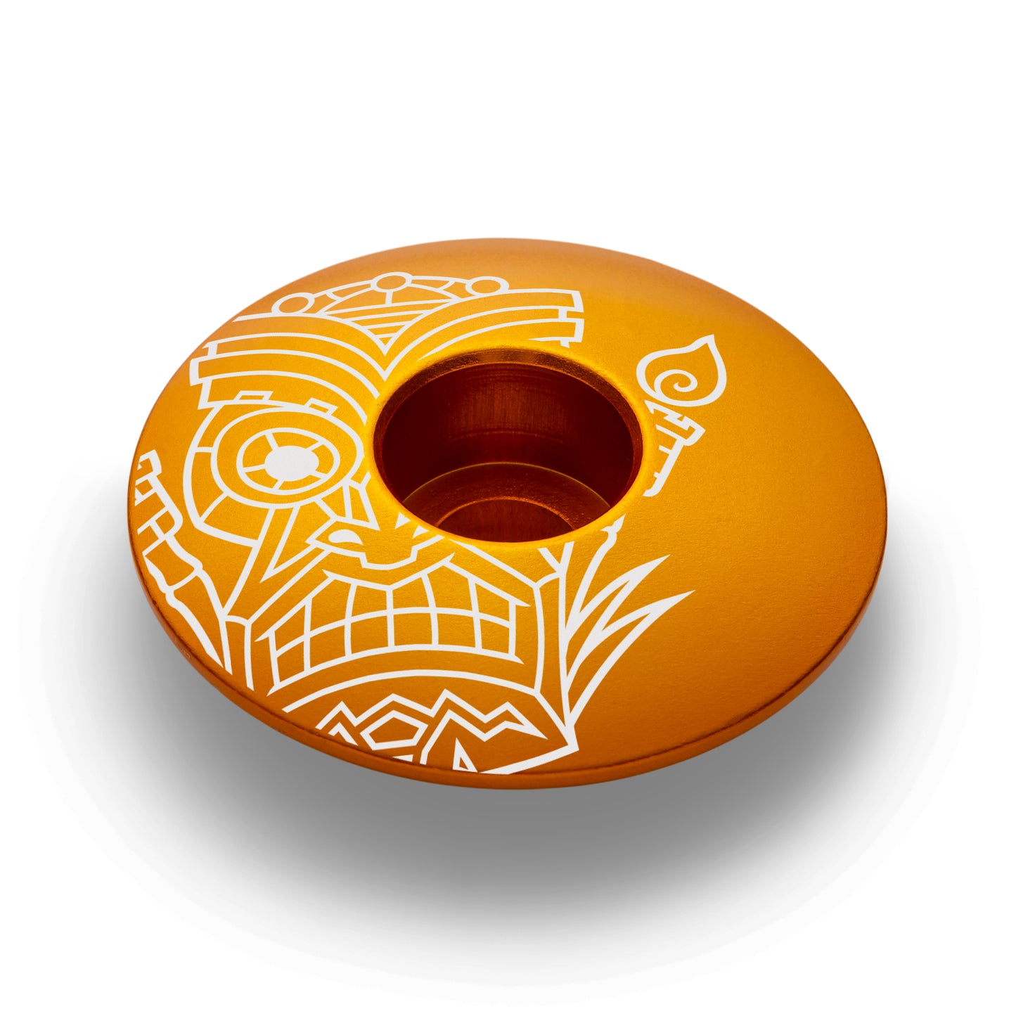 Gold bike headset top cover with a tiki design made of lightweight and durable aluminum.