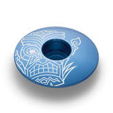 Blue bicycle stem cap showcasing a tiki-inspired design compatible with 1 1/8-inch steerer tubes