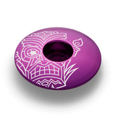 Purple bike stem cap showcasing a tiki-inspired design for 1 1/8-inch steerer tubes.